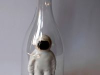 Ceramiczna figurka kosmonauty w białym kombinezonie. Zamknięta w plastikowej butelce.