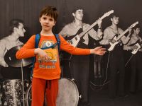 Chłopiec pozuje na tle czarno-białego archiwalnego zdjęcia z grupa muzyczną z PM