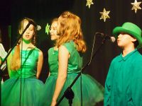 dziewczynki i chłopak w zielonych strojach przy mikrofonach.